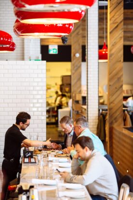 people sitting at a pizza bar table with a waiter showing them the menu