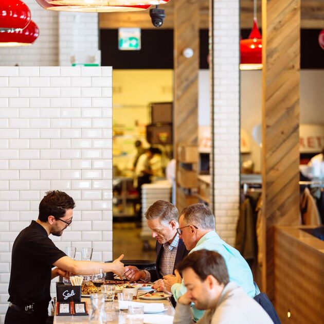 people sitting at a pizza bar table with a waiter showing them the menu