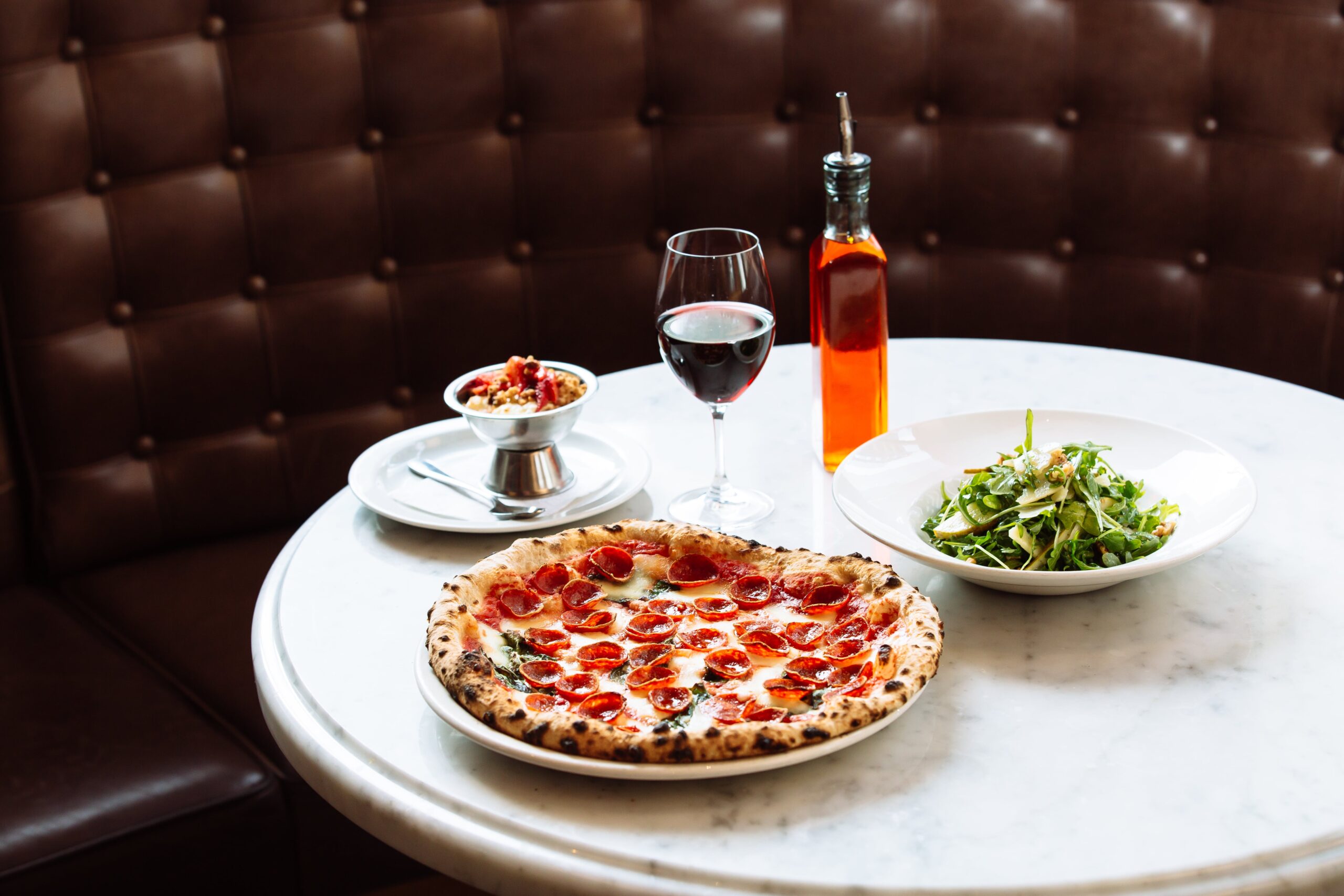 table with salad, pizza, dessert, and glass of wine